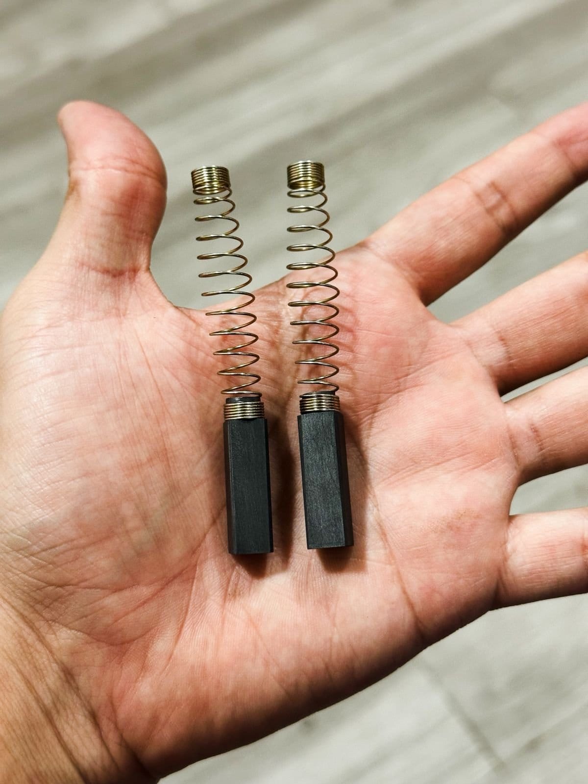 Carbones para descremadora Elecrem sostenidos en la mano, con su resorte de cobre